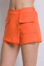 Bright orange women's cargo skorts with functional pockets, showcased on a model against a plain background.