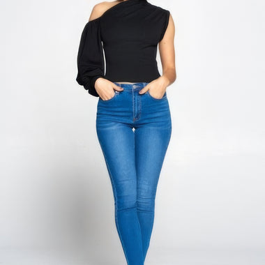 Stylish one-shoulder black blouse, slim-fit blue denim jeans, bare feet model posing in studio