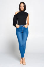 Stylish one-shoulder black blouse, slim-fit blue denim jeans, bare feet model posing in studio